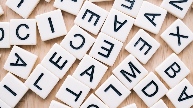 A close-up of scattered letter tiles on a wooden surface, captured from above.
