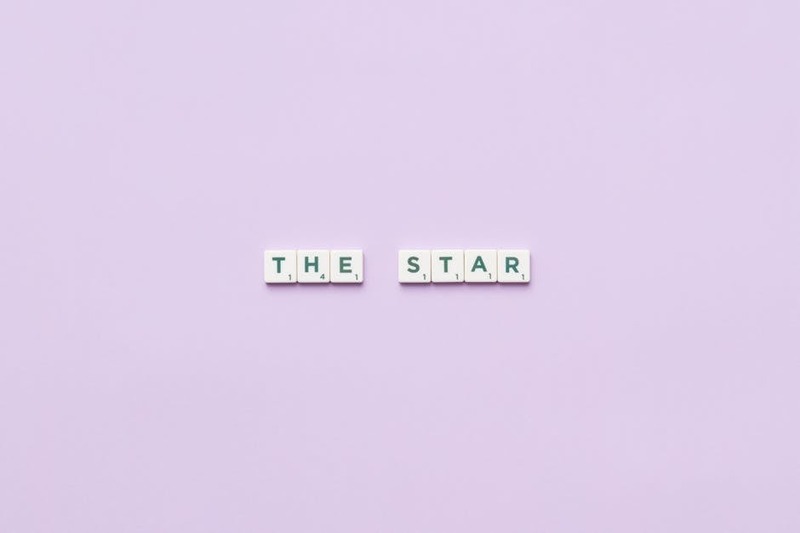 Scrabble tiles spelling 'The Star' on a soft pastel background, providing clean copy space.