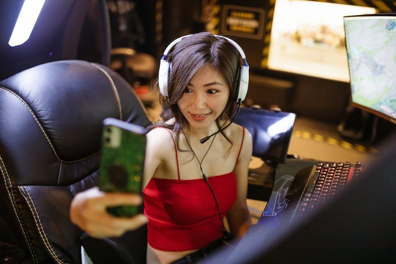 A female streamer smiling and talking while looking at her chat on a second monitor, playing a vibrant video game.